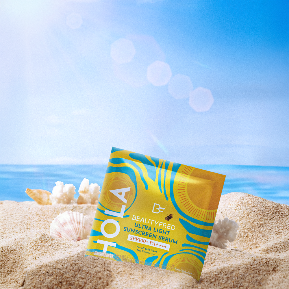 HOLA! Beautyified sunscreen serum packet on sand with ocean and sky background