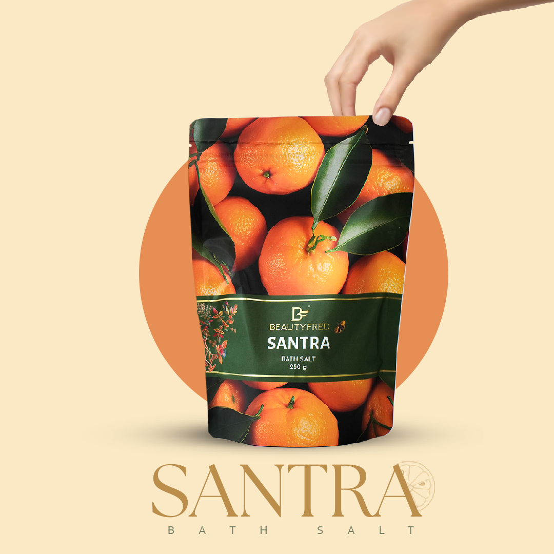 Hand holding a bag of Beautyfred Santra bath salt with orange design on a beige background